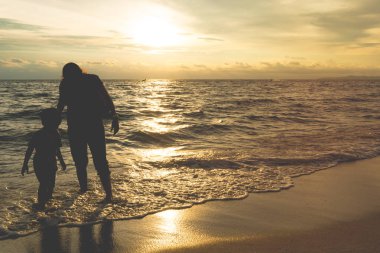 Anne ve oğlu altın günbatımı kumsalda oynarken siluet gölge