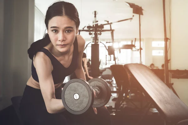 Strong Asian skinny woman is lifting dumbbell in fitness