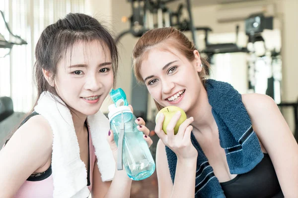 Sport women is drinking water and eat apple while exercising in fitness