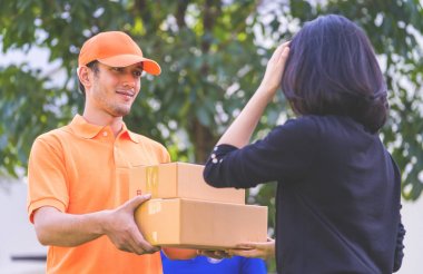 Turuncu elbiseli teslimatçı bir kadına paket teslim ediyor.