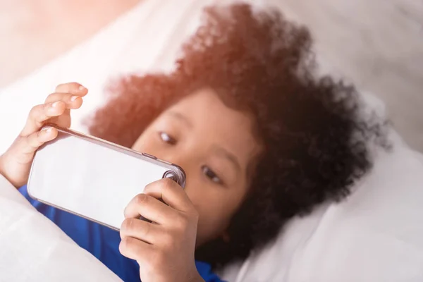 Niño pequeño está jugando con el teléfono móvil en la cama —  Fotos de Stock