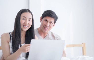 Mutlu Asya çift dizüstü sabah yatakta gülümseme ile kullanma