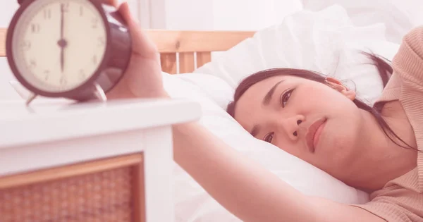 アジアの女性の目覚まし時計を停止する手を差し伸べるベッドの上 — ストック写真