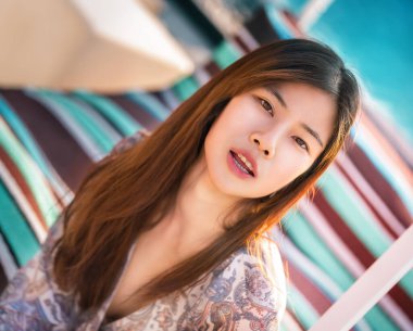 Şehvetli, güzel Asyalı kadın plaj kenarında bir kanepede oturuyor. Tatil ve gevşeme için..