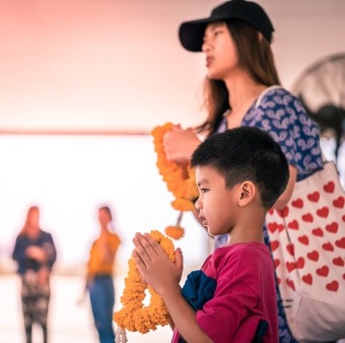 Taylandlı anne ve kızı Budizm için çiçek çelengiyle dua ediyor. İyi şanslar ve ruhani inanç. 