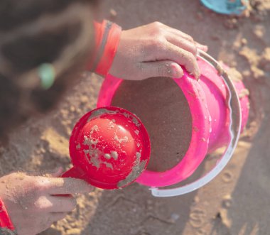 Çocuk yaz tatili oyuncağı konsepti için kum dolu renkli pembe plastik kovayla oynuyor..