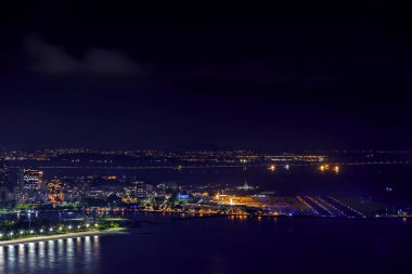 Gece şehir ışıkları, binalar ve Rio Niteroi Köprüsü'nde arka plan ile Rio de Janeiro Santos Dumont havaalanına üstündeki görünümünü