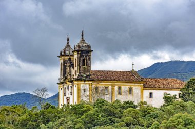 Antik tarihi kilise yüksek birinde birkaç dağlar bitki örtüsü ve arka planda karanlık bulutlar Ouro Preto'daki şehir