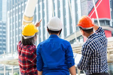 Asya mühendisleri grup planı kağıt basılı tutarak çalışma sitesi yapı inşaat bakın. Şehir kavramı içinde arka plan, iş, Bina, ekip çalışması, jest ve insanlar. ekip çalışması kavramı