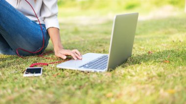 Kız müzik dinlemek ve bir kitap okuma zevk ve dizüstü (yeşil tonu sabah parkta çim sahada oynamak