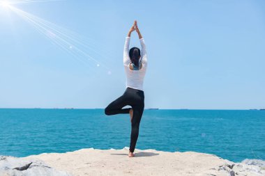 Gün doğumunda sahilde yoga yapan genç bir kadın.