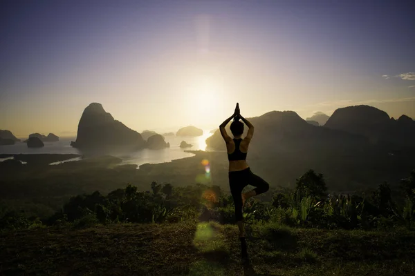 Silhouette young woman practicing yoga on swimming pool and the beach at sunset.