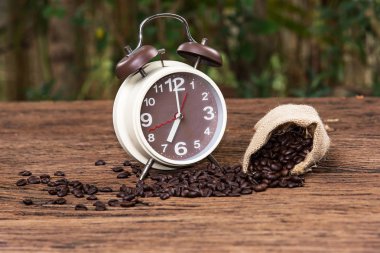 Seçici odak noktası Vintage getirilmiş saat yüzü ve çuvaldaki kahve çekirdeği arka plandaki ahşap masaya düşüyor. Rahatlamak için kahve molası. Eski tarz efekt resimleri..