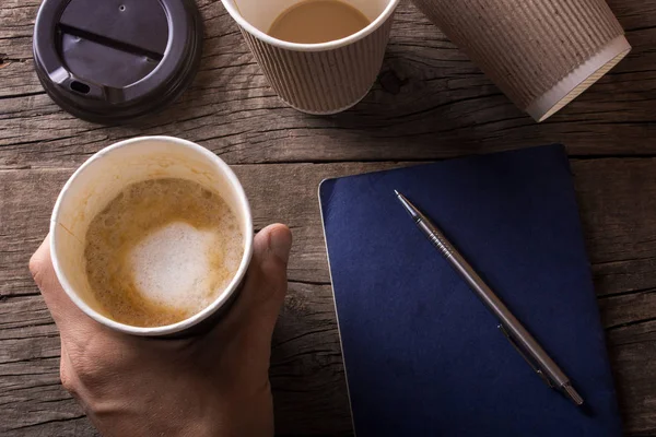 Adam kahve bir elinde tutan, masanın üzerinde bir not defteri yalan ve — Stok fotoğraf