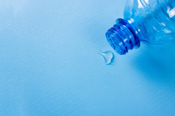 Druppels van zuiver water gemorst uit een fles op een blauwe achtergrond. — Stockfoto