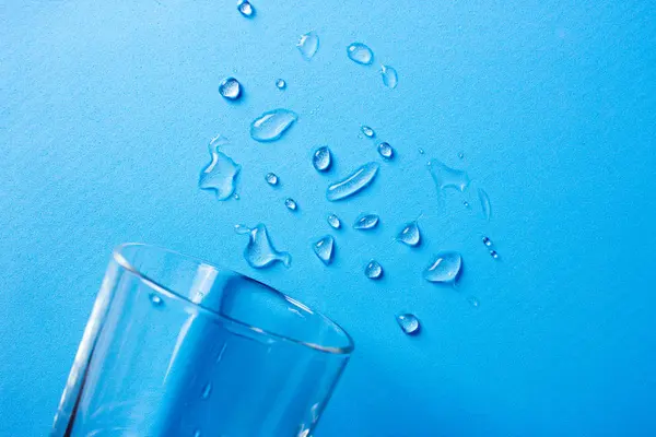 Gotas de água pura derramadas de um copo em um fundo azul — Fotografia de Stock