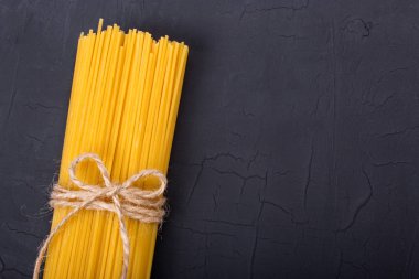 Siyah bir zemin üzerine çiğ sarı uzun spagetti yığını. Hamur metin mockup için kopya alanı