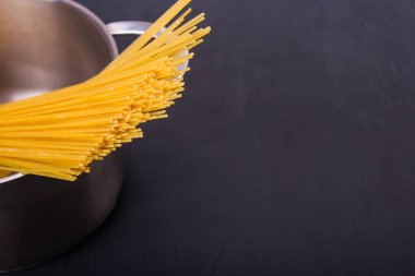 Siyah bir arka üzerinde bir tencerede çiğ sarı uzun spagetti yığını