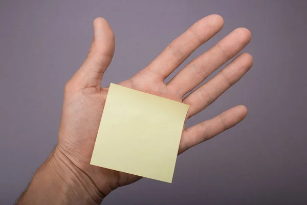 Poznámka: nálepka žlutého papíru v ruce na šedém pozadí moc — Stock fotografie