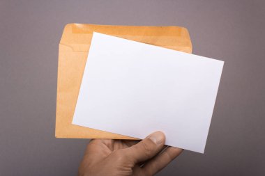 Boş kartpostal ve broşür gri arka plan üzerinde elinde zarf