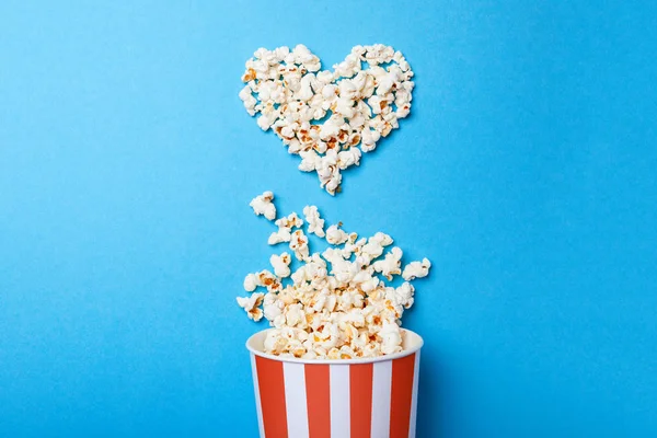 Ich schaue gerne Filme. verschüttetes Popcorn in Herzform und Papiereimer in einem roten Streifen auf blauem Hintergrund. — Stockfoto