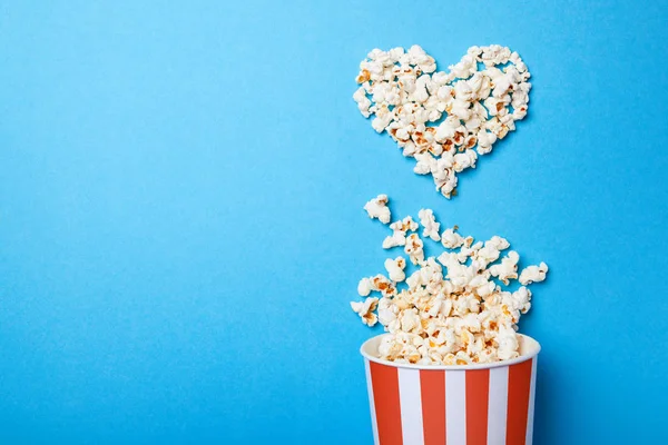 Ich schaue gerne Filme. verschüttete Popcorn in Herz- und Papiereimerform in einem roten Streifen auf blauem Hintergrund. Kopierraum für Text — Stockfoto