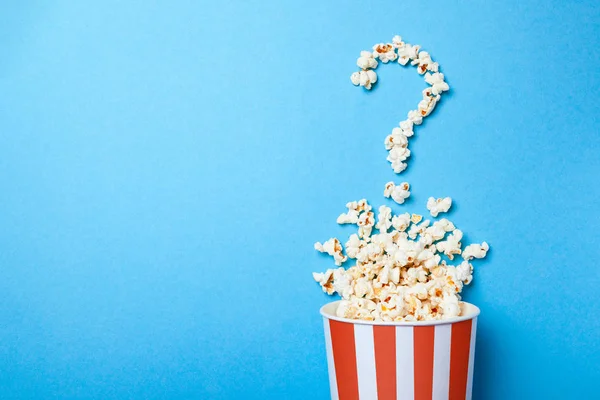 Konzept, für welchen Film man sich entscheiden sollte. verschüttetes Popcorn in Form von Fragezeichen und einem Papiereimer in rotem Streifen auf blauem Hintergrund. Kopierraum für Text — Stockfoto
