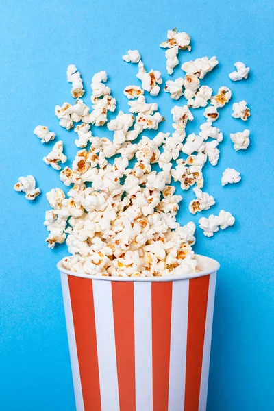 Palomitas de maíz derramadas y cubo de papel en tira roja sobre fondo azul. Copiar espacio para texto — Foto de Stock