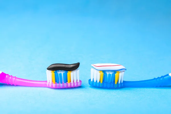 Whitening toothpaste is usual colored and black from charcoal on toothbrush. Concept. Which toothpaste to choose? How to whiten your teeth? — Stock Photo, Image