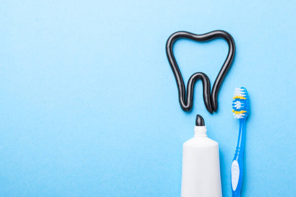 Black toothpaste from charcoal for white teeth. Toothpaste in the form of  tooth,  tube and  toothbrush on  blue background. Copy space for text