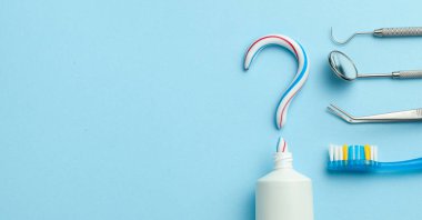 Diş macunundaki soru işareti. Renkli diş macunu, diş fırçası, dişçi aletleri, ayna, mavi arka plan kancası. Dişlerini fırçalamak için iyi bir diş macunu seçmen. Boşluğu kopyala