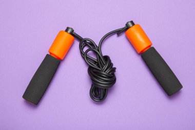 İp atlama. Vücut sağlığı için eğlenceli egzersizler. Siyah kordonlu turuncu ip. Mor arkaplan