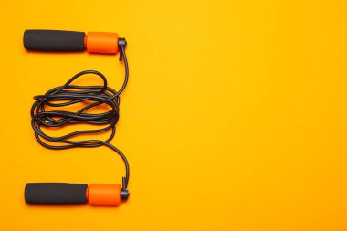 İp atlama. Vücut sağlığı için eğlenceli egzersizler. Siyah kordonlu turuncu ip. Sarı turuncu arkaplan