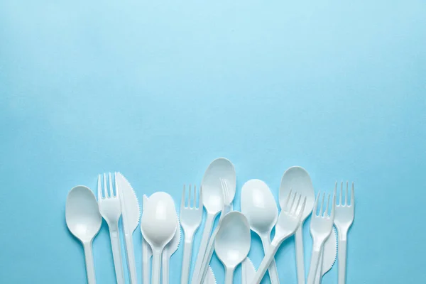 Plastic cutlery, forks, spoons and knives. Pollution of the environment with plastic and microplastics. Blue background. Copy space for text.