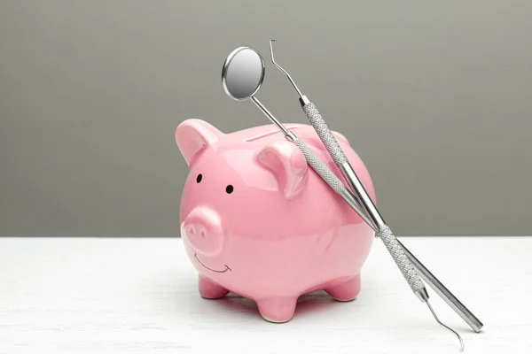 Pink piggy bank and dental tools on gray background. The concept of how to save on dental treatment — Stock Photo, Image