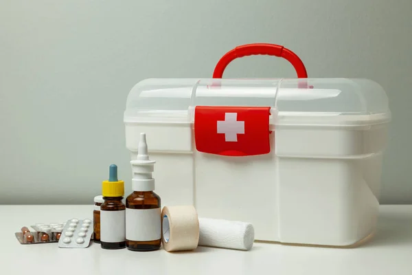 Kit de primeiros socorros. Caixa branca com uma cruz e um fixador vermelho e comprimidos com garrafas de medicamentos em um fundo cinza — Fotografia de Stock