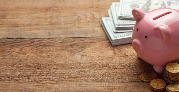 Hucha rosa y dinero con billetes y monedas en una mesa de madera. Copiar espacio para texto . —  Fotos de Stock