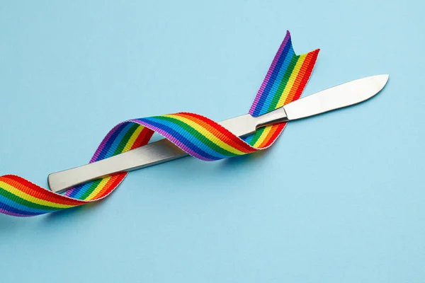 Scalpel y el arco iris LGBT símbolo del orgullo de la cinta. Operación de cambio de sexo. Fondos azules — Foto de Stock