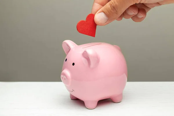 Spenden von Liebe und Gefühlen, Mitgefühl. Mann legt Herz in Sparschwein — Stockfoto