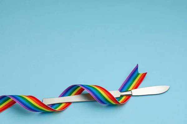Scalpel and rainbow LGBT ribbon pride symbol. Sex change operation. Blue background. Copy space for text. — стокове фото