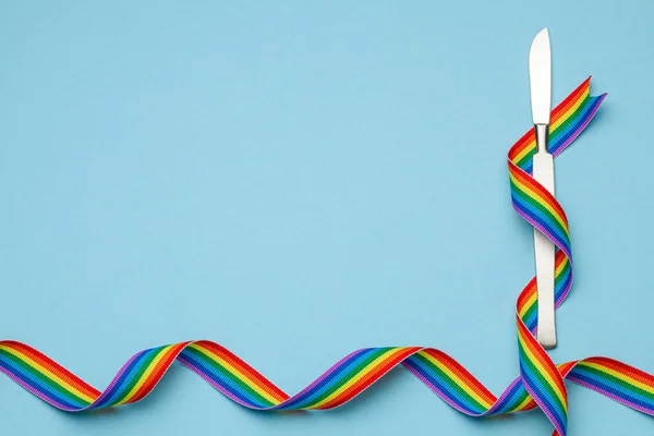 Bisturi e arco-íris símbolo orgulho fita LGBT. Operação de mudança de sexo. Fundo azul. Espaço de cópia para texto . — Fotografia de Stock