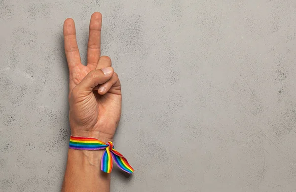 Barış ve zaferin sembolü iki parmaktan. Gri arka plan. Lgbt gökkuşağı kurdele gururu. Metin için alanı kopyala.
