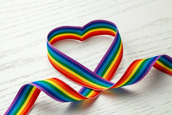 Fita de arco-íris LGBT em forma de coração. Símbolo do orgulho. Fundo de madeira branca — Fotografia de Stock