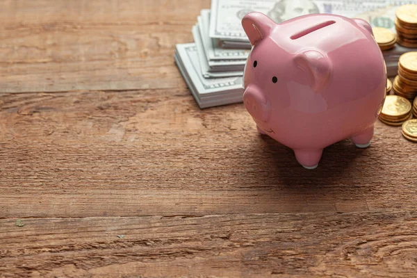 Rózsaszín malacpersely és pénz bankjegyekkel és érmékkel egy fa asztalon. A szöveg másolási helye. — Stock Fotó