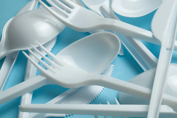 Plastic cutlery, forks, spoons and knives. Pollution of the environment with plastic and microplastics. Blue background