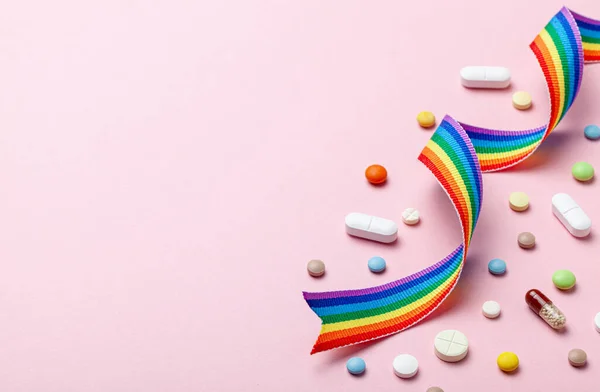 Pastillas hormonales después del cambio de sexo. Transición transgénero. Travesti. Orgullo LGBT arco iris cinta y pastillas sobre fondo rosa . — Foto de Stock