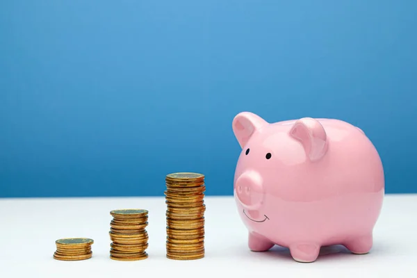 Hucha rosa y una pila de monedas en los escalones sobre una mesa de madera y fondo azul — Foto de Stock