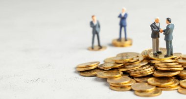 İşadamları, başarılı kârlı bir işlemin sembolü olarak el sıkışıyor. Başarı veya başarılı yatırımların sembolü olarak altın sikke yığını üzerinde Işadamları
