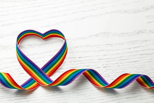 Cinta de arco iris LGBT en forma de corazón. Símbolo de cinta de orgullo. Fondo de madera blanca. Copiar espacio para texto. — Foto de Stock