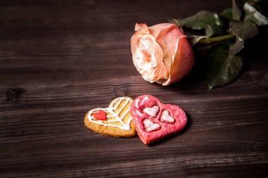2 heart-shaped cookies for Valentine's Day on a dark wood background with one pink rose